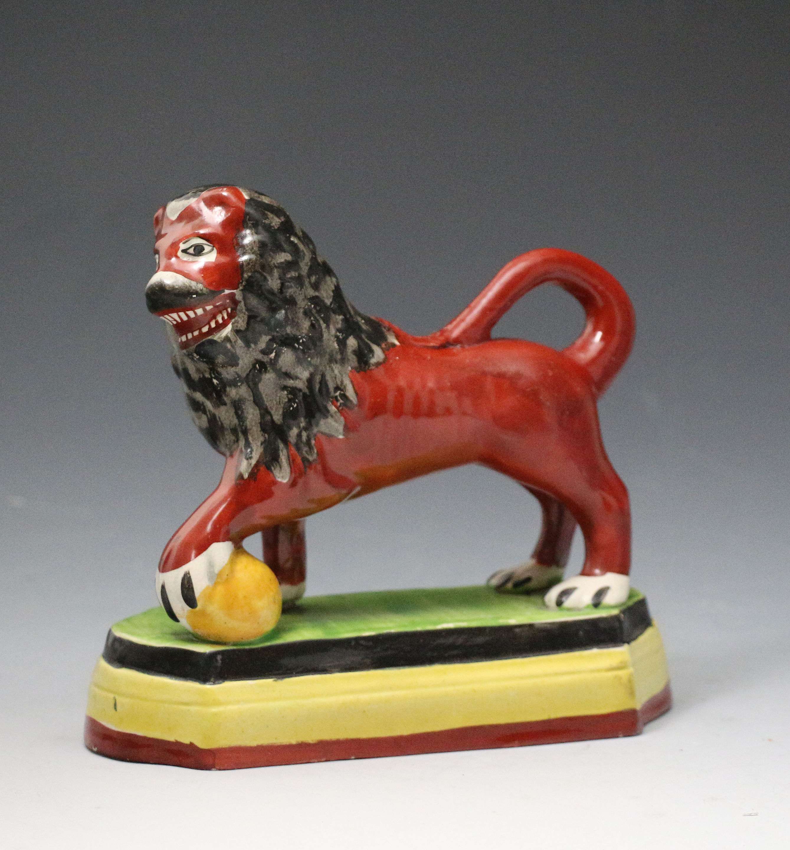 Antique Staffordshire pottery figure of a lion on a base with paw on ball early 19th century